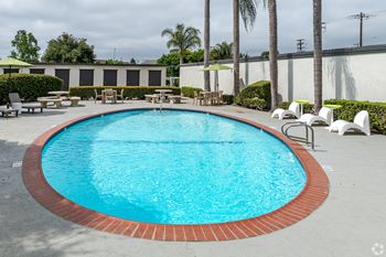 A rectangular pool with a red border and white chairs around it.
